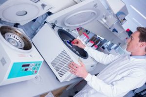 Chemist in lab coat using a centrifuge in laboratory